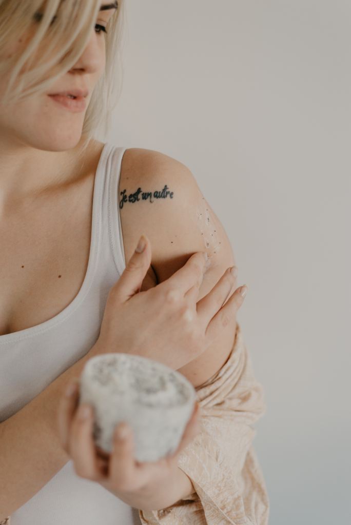 A caucasian women is wearing a white vest and running an exfoliating balm on her left arm. A tattoo saying 'Je est un autre' (French for 'I am another') is visible near her shoulder.

Pandora's Health blog